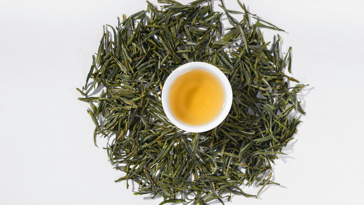 Cup of freshly brewed green tea with loose leaf green tea around the cup