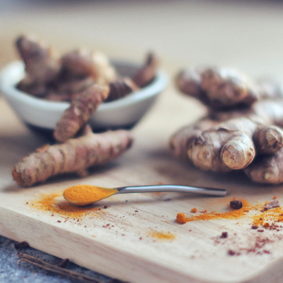 Turmeric root on a wooden board with a spoonful of turmeric powder.