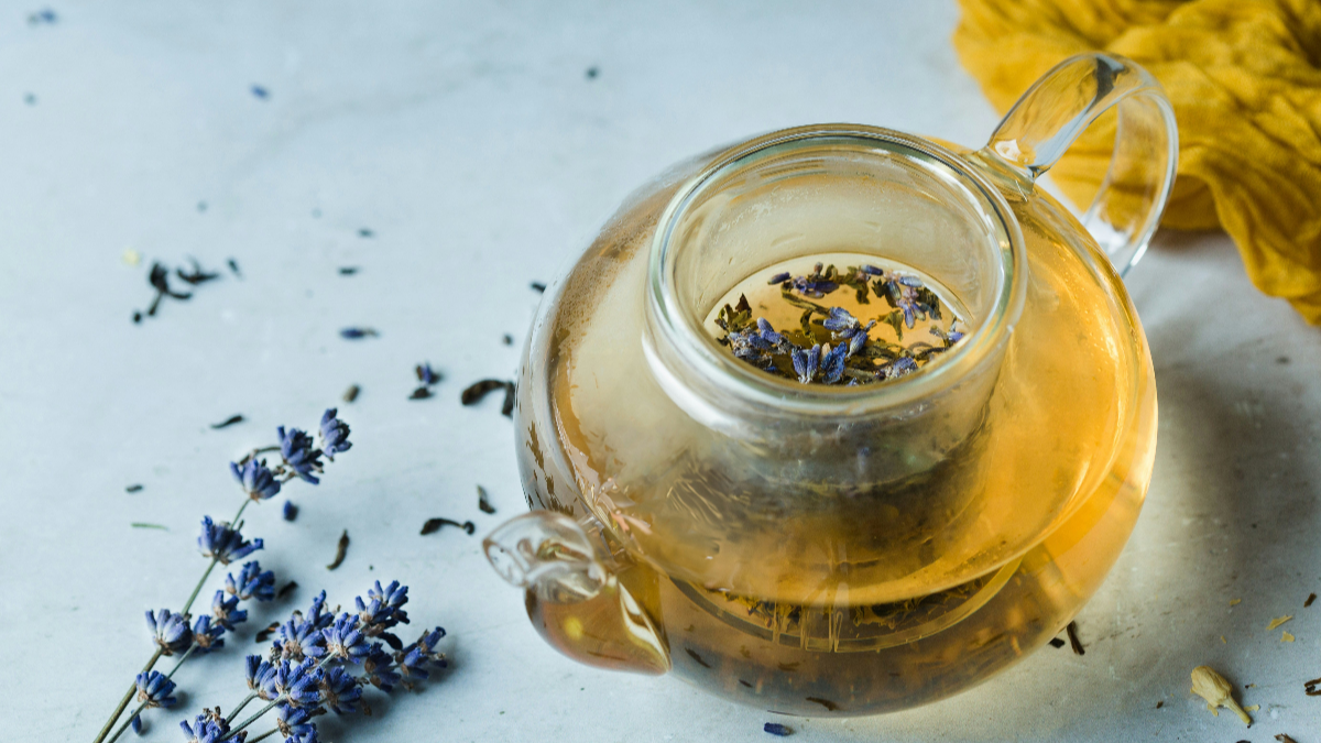 Glass teapot with lavender flowers on a light surface