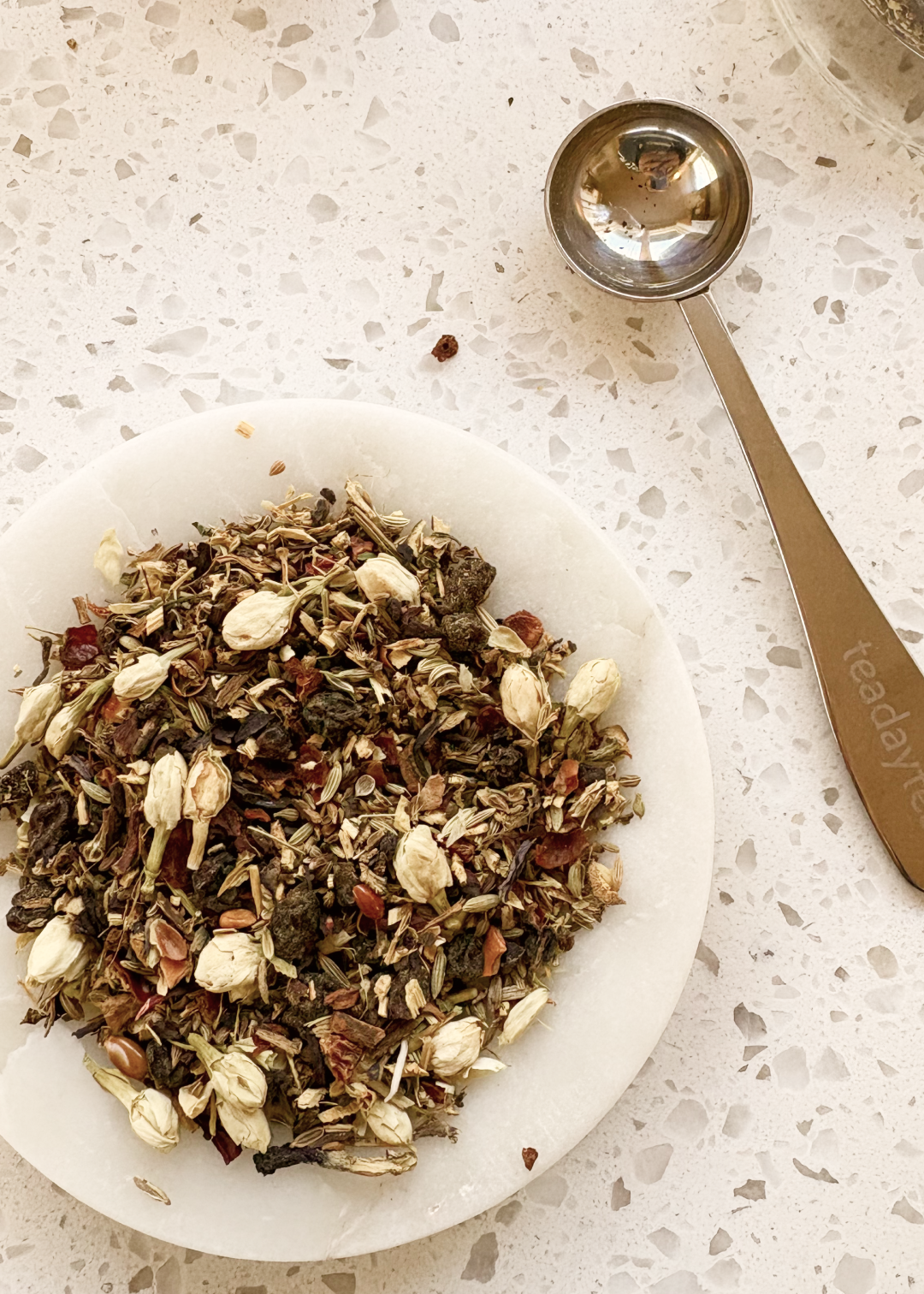 Blue Butterfly Digestif tea leaves in a bowl with a measuring spoon on a speckled surface.