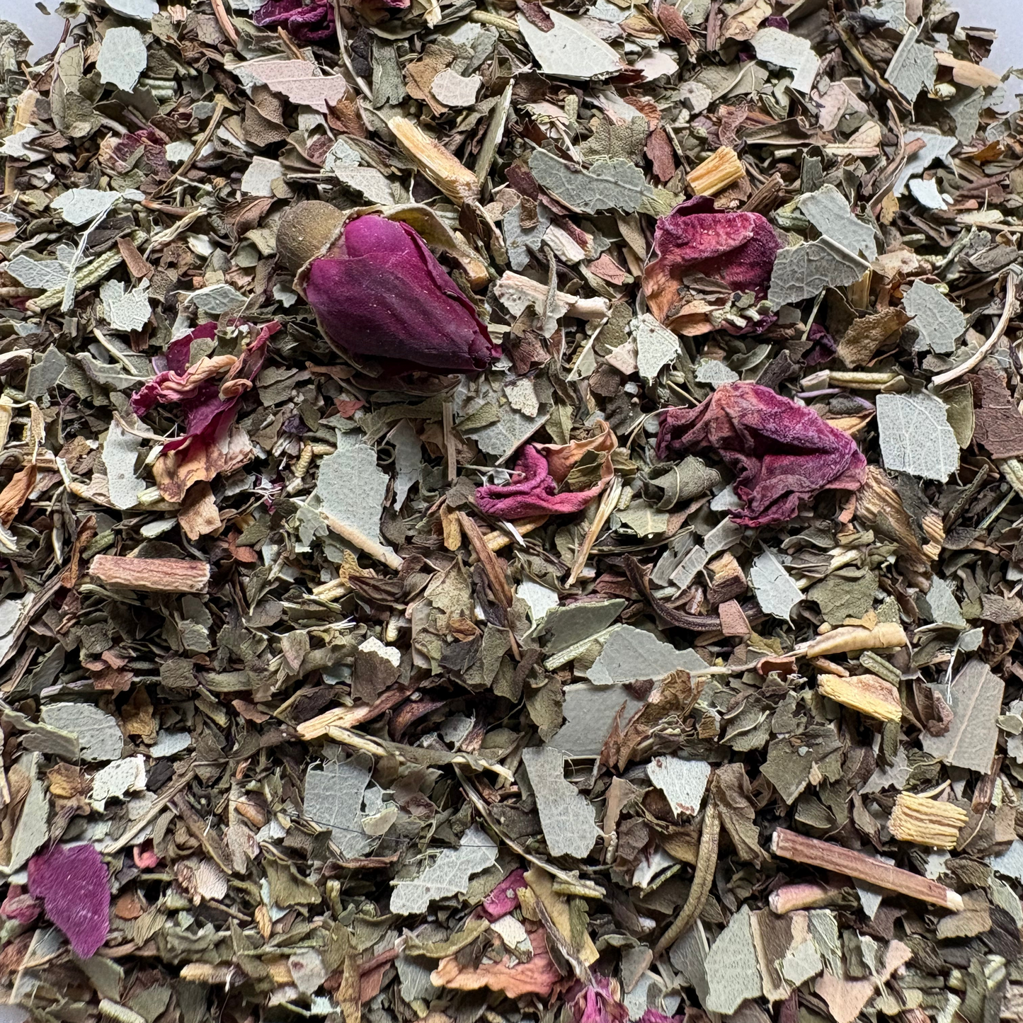 A detailed close-up of the loose-leaf Breathe Easy herbal tea blend, featuring a base of dried green mint and eucalyptus leaves mixed with woodier rosemary pieces, scattered pink and deep magenta rose buds, and delicate rose petals.