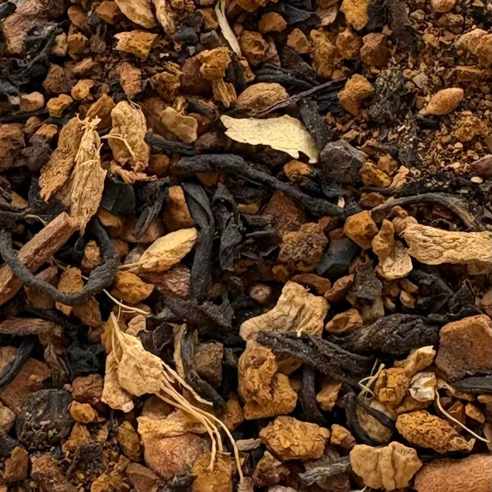 A macro close-up of Chaga Vanilla Chai loose leaf tea, showing the contrast between dark Assam tea leaves, woody Chaga mushroom chunks, and fragments of ginger and cinnamon spices.