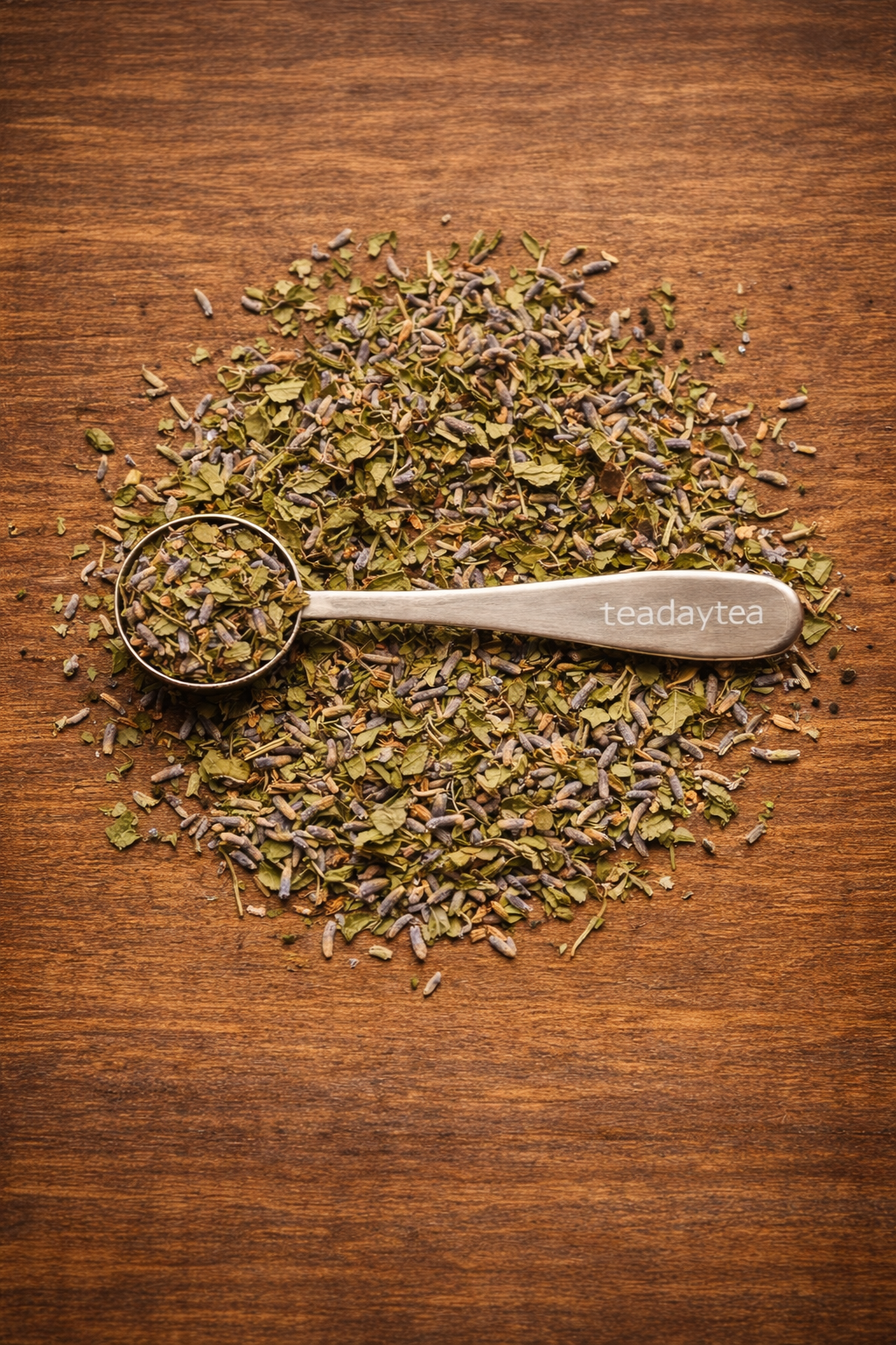 Dry peppermint leaves and lavender flowers with a metal scoop on a wooden surface.