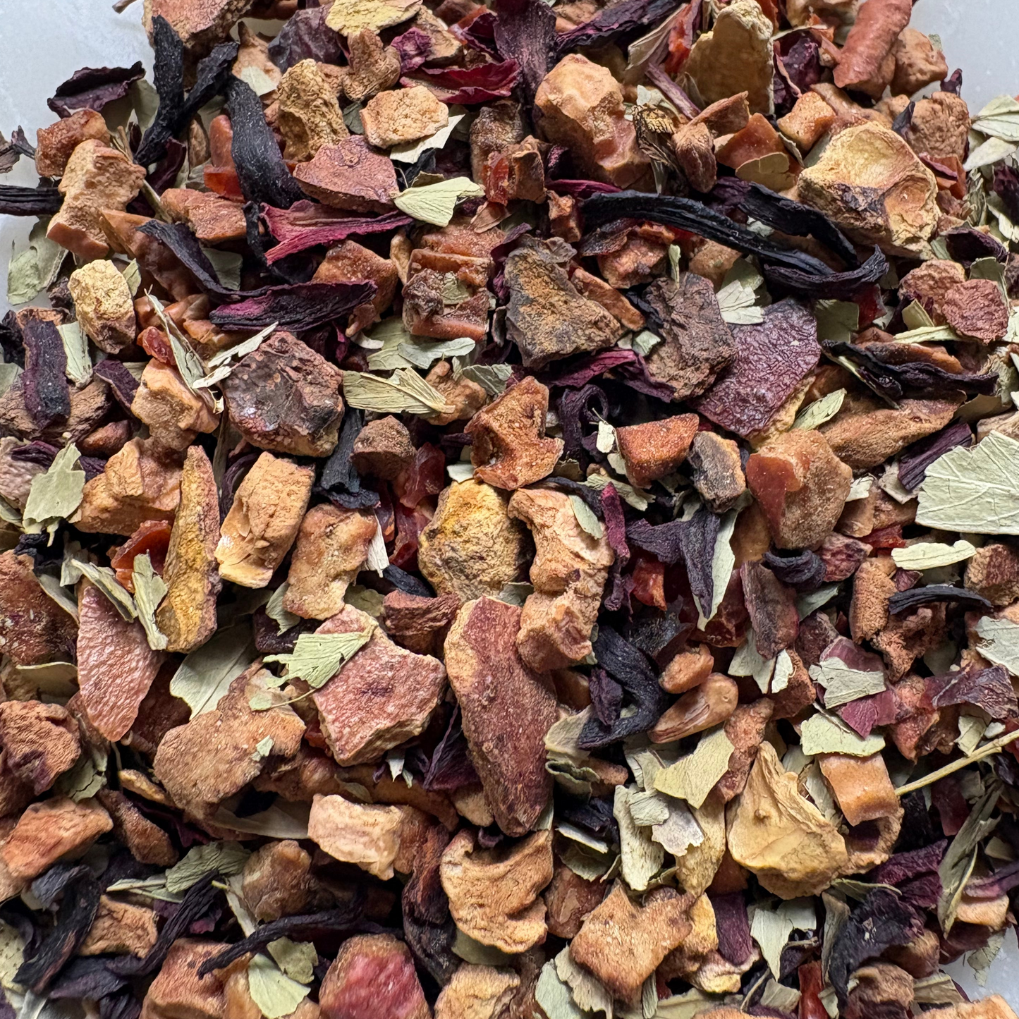 A rich, colorful close-up of the loose-leaf Let It Go - Colon Cleanse herbal tea blend, showcasing a textured mix of large dried apple pieces, deep red hibiscus petals, and scattered green botanical leaves piled on a white surface.