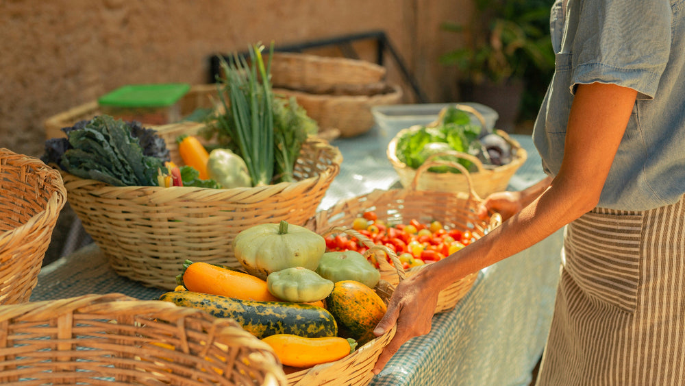 Person arranging vegetables on a table with baskets of produce
