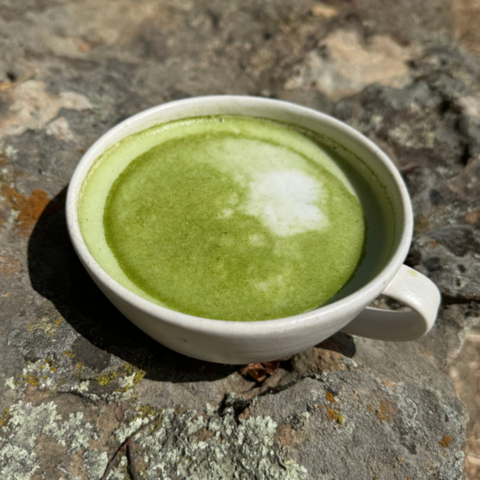 White cup of green matcha tea on a stone surface