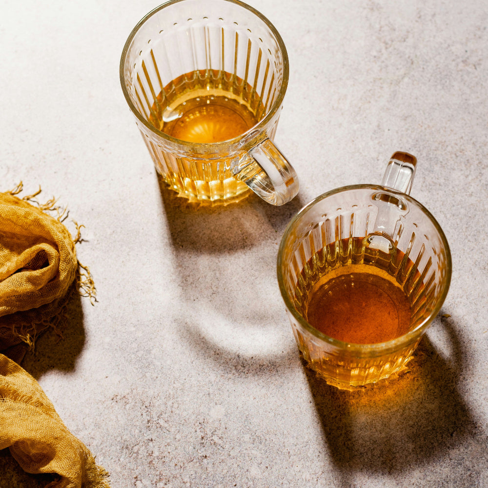 Two glass cups filled with a golden liquid on a textured surface with a yellow cloth.