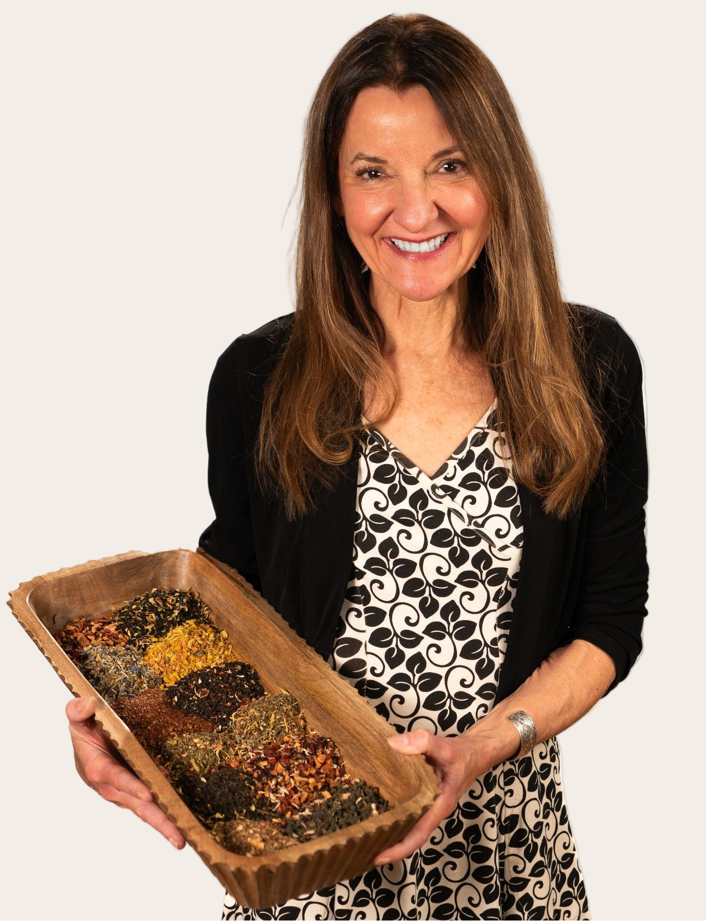 Nicole Carrol, owner & founder of Teadaytea, holding a wooden tray with various seeds or grains against a white background