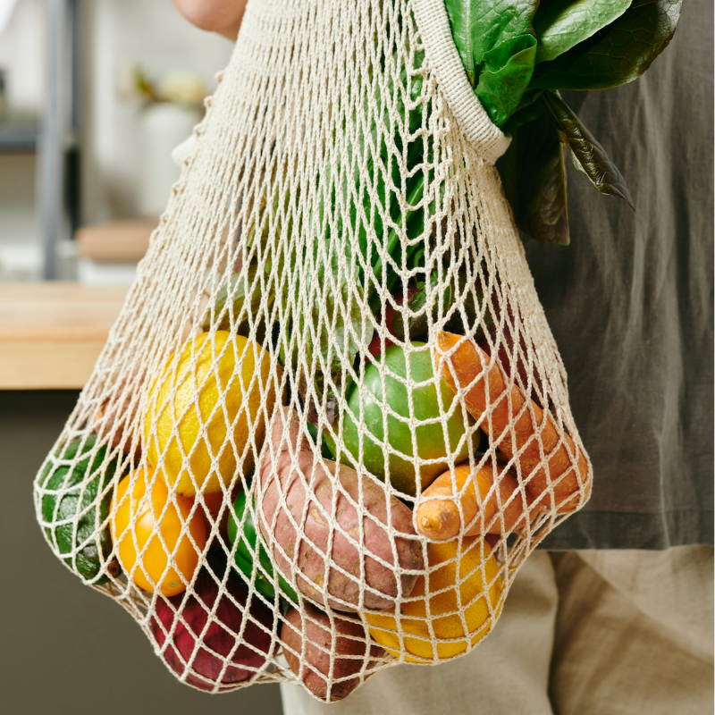 Net bag filled with fruits and vegetables held by a person.