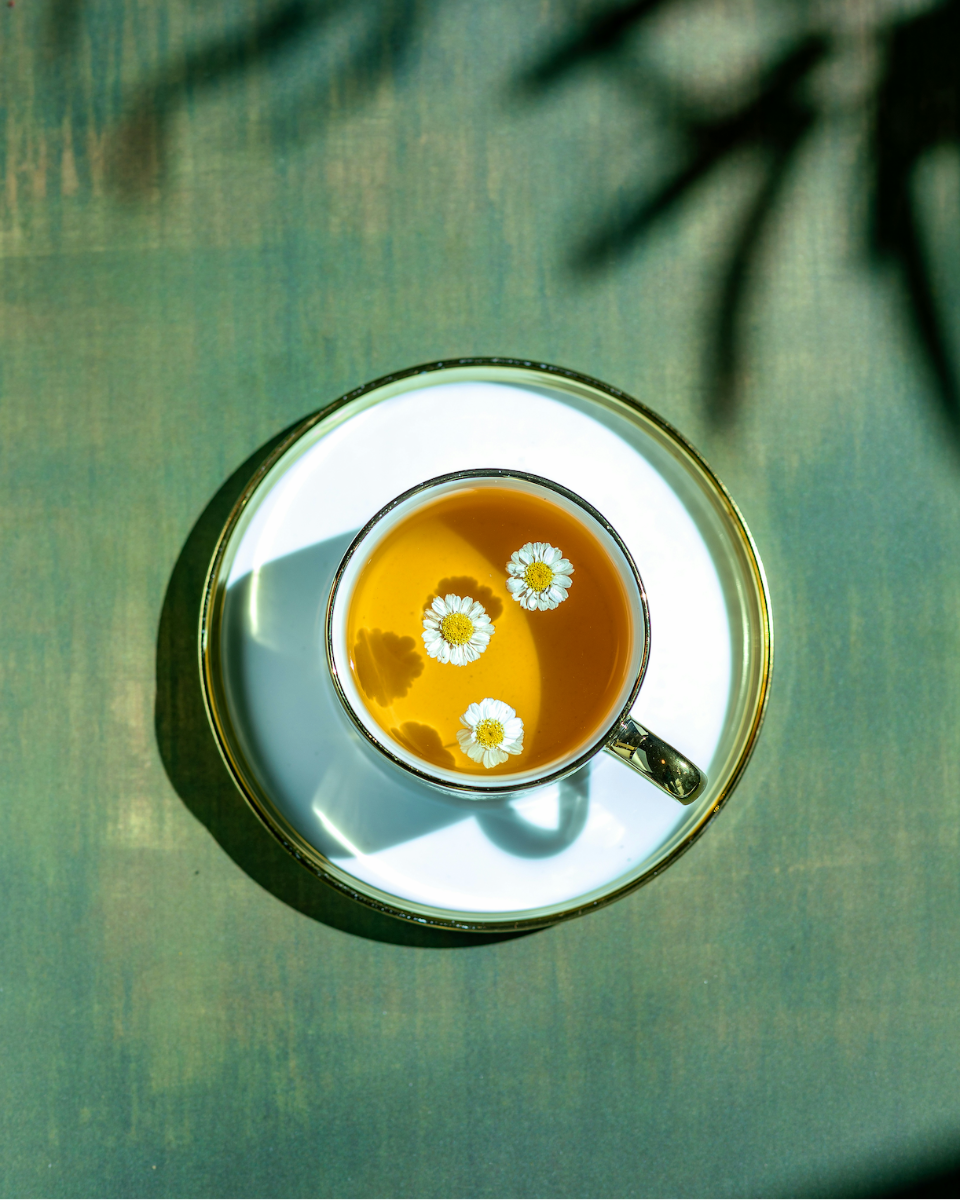 Teacup with daisies on a reflective surface, with a blurred natural background