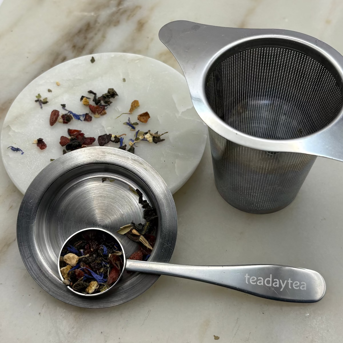 Tea-making set with tea leaves, spoon, and strainer on a marble surface
