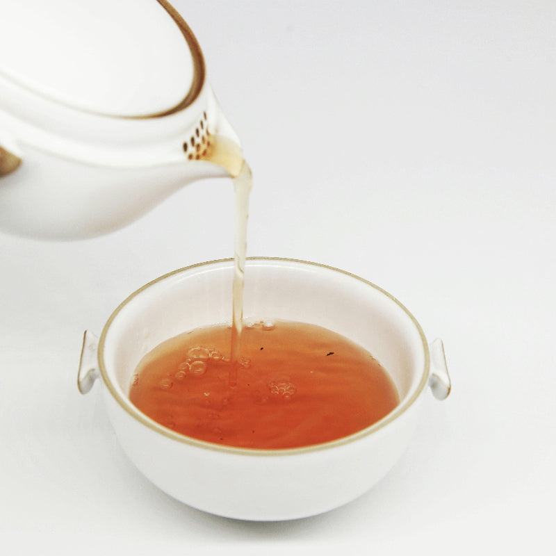 Tea being poured from a white teapot into a white cup on a light background