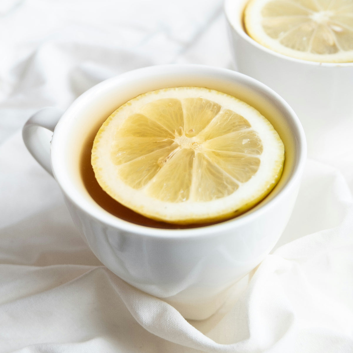 White mug with lemon slice and honey being drizzled, on a white fabric background