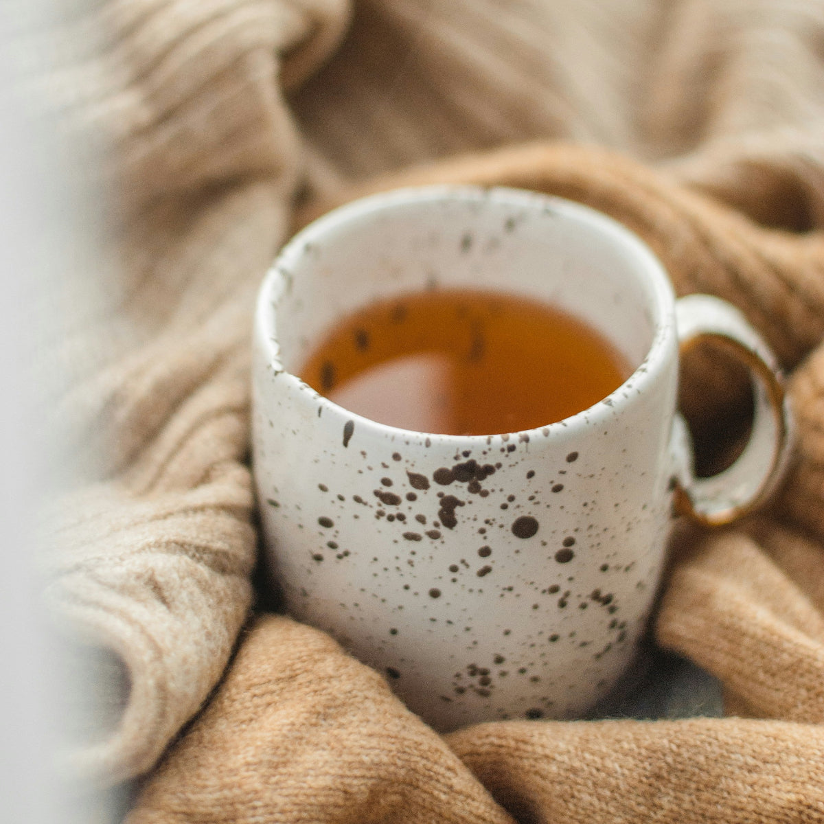 White speckled mug with tea on a soft beige blanket