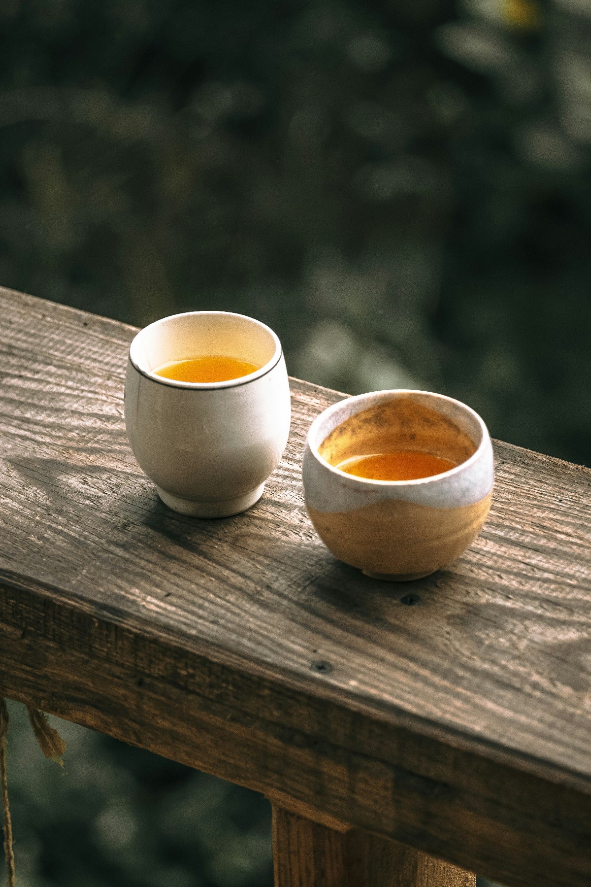 Two ceramic cups with tea on a wooden surface outdoors