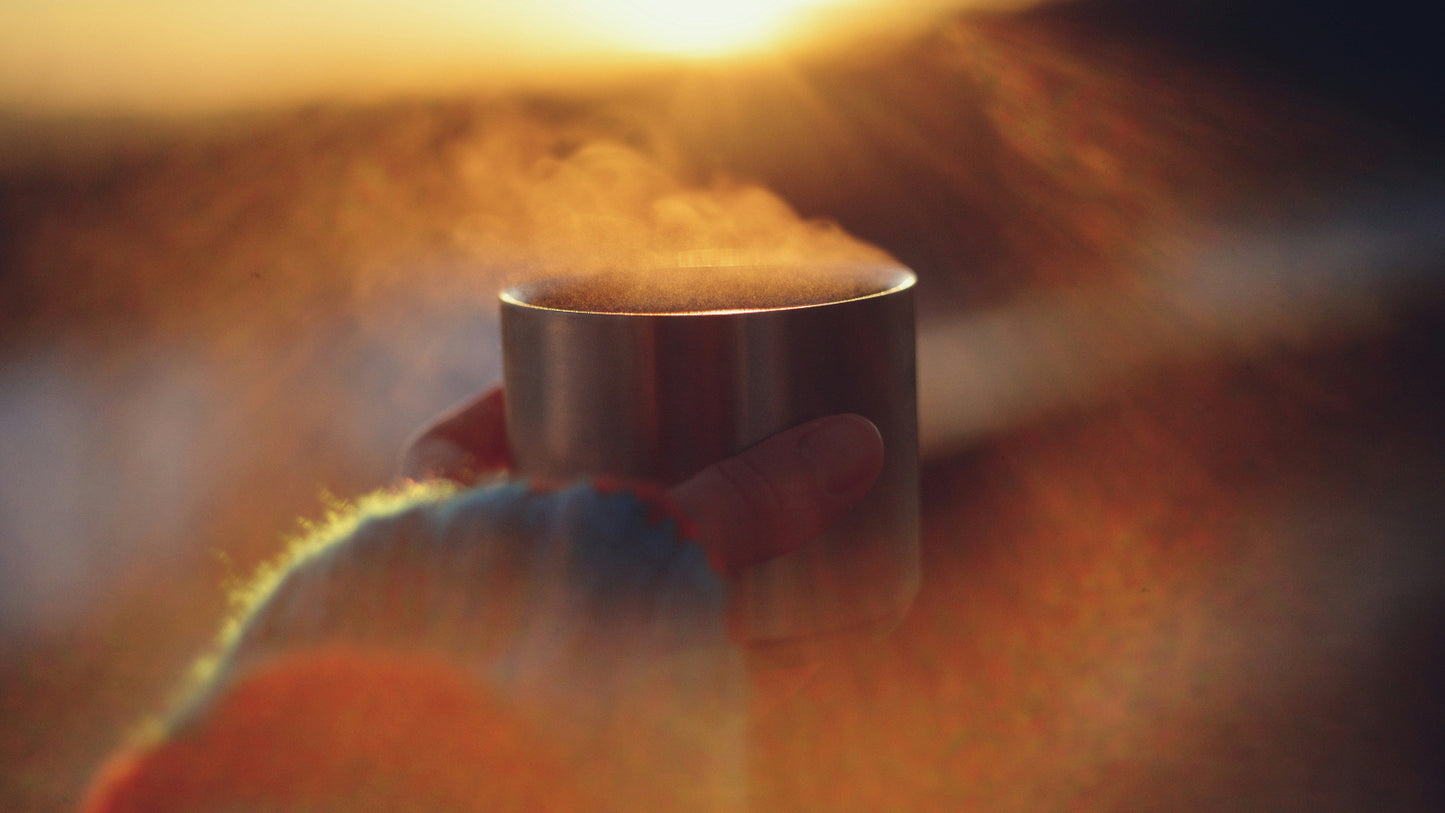 Hand holding a steaming cup with a warm, blurred background