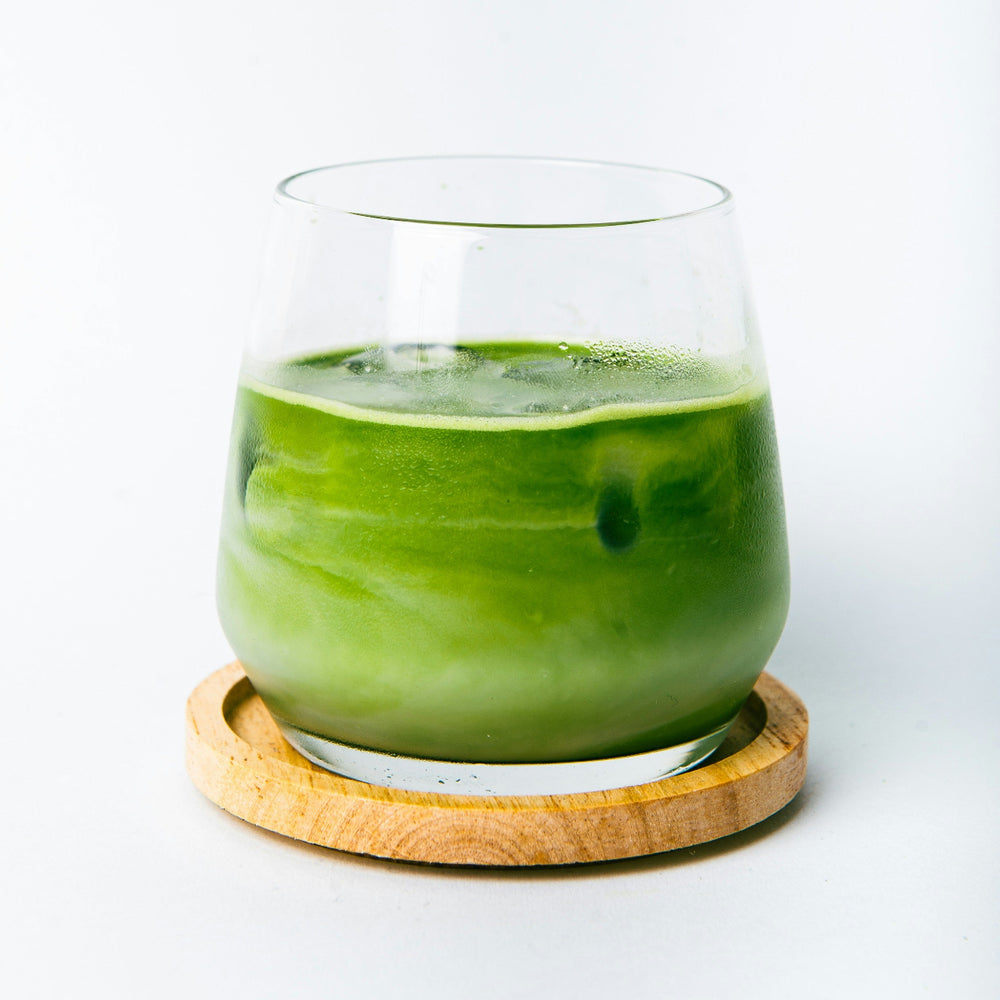 
                  
                    Glass of iced matcha on a wooden coaster with a white background
                  
                