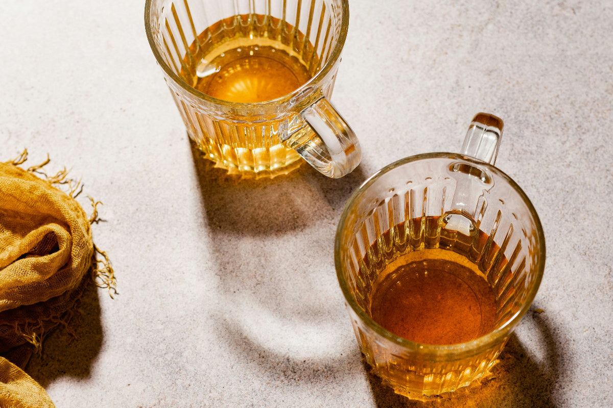 Two glass cups filled with tea on a textured surface with a yellow cloth.