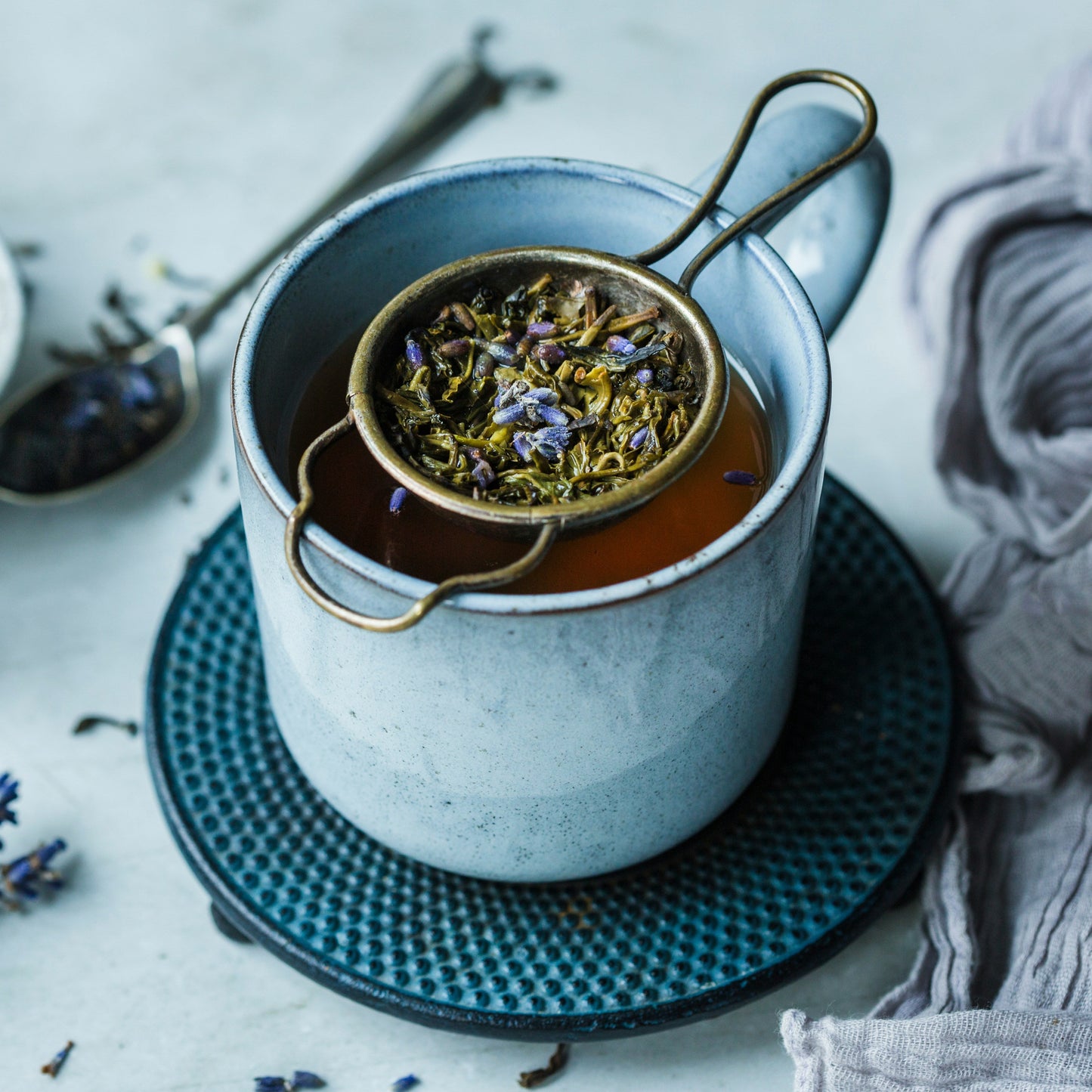 Tea cup with lavender flowers and a strainer on a textured surface
