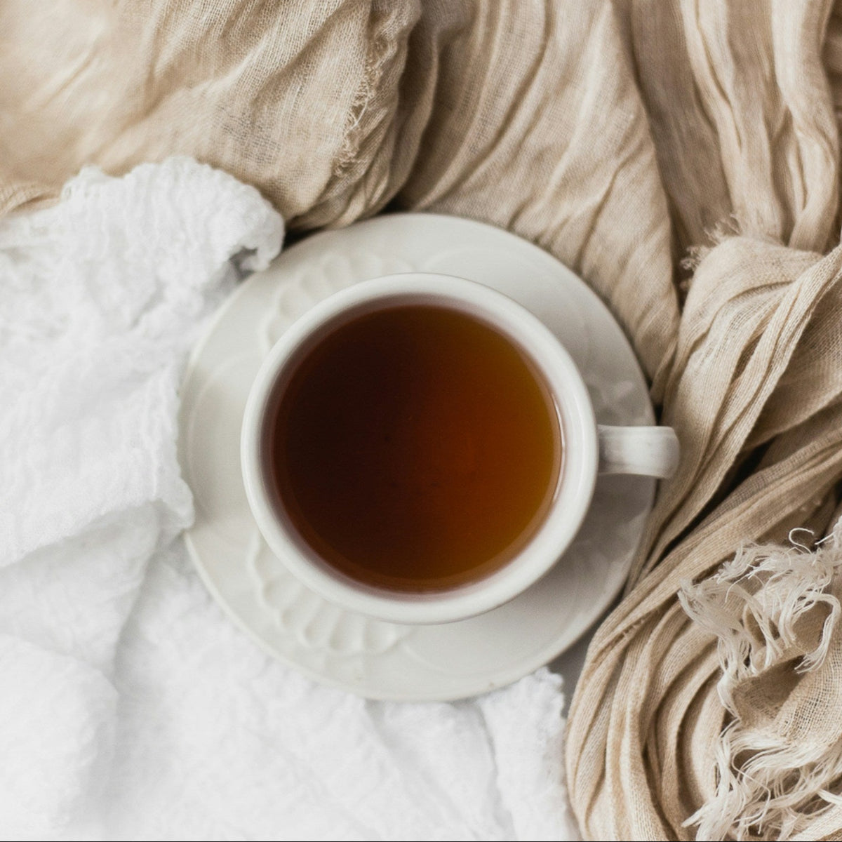 White cup of tea on a white surface with beige fabric