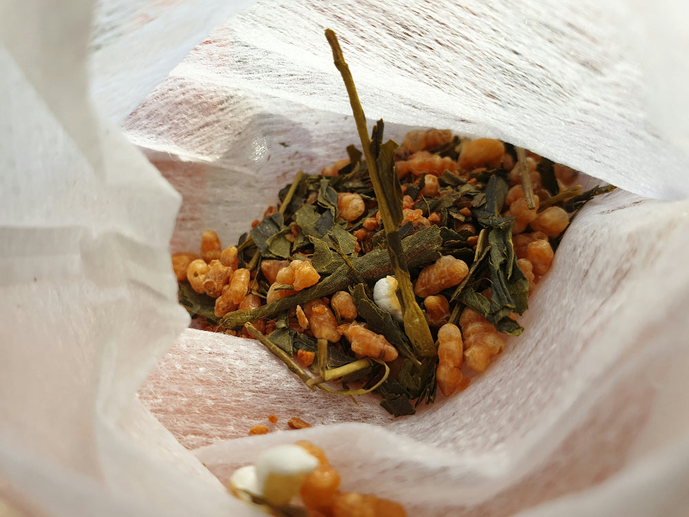 Tea leaves and small orange pieces in a white fabric bag