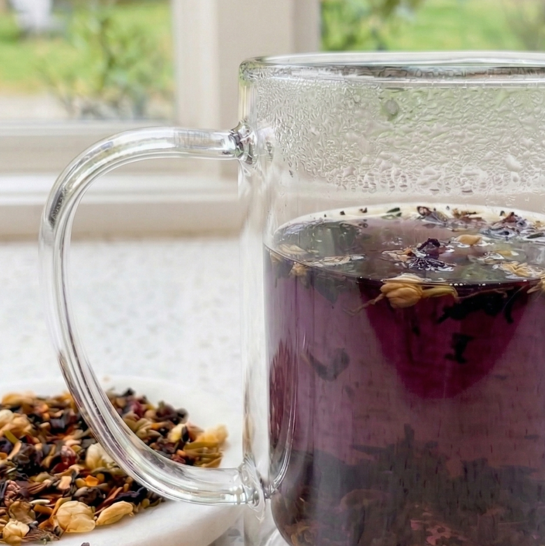 Steeped Blue Butterfly Digestif herbal tea in a clear double-walled glass mug, featuring a vibrant purple color and loose tea leaves.