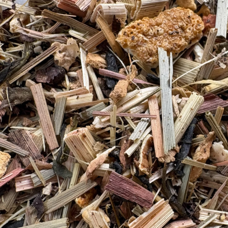 A high-quality overhead view of loose-leaf Man Tea, showing a textured blend of dried organic lemongrass, green tea leaves, eleuthero root, and orange peel.