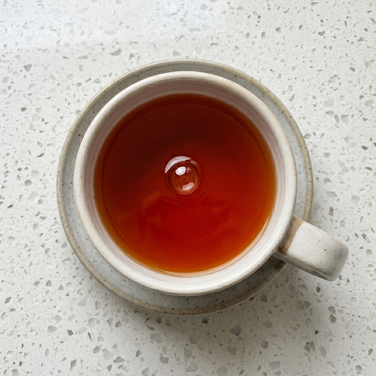 Golden herbal tea steeped in tea cup on speckled surface. 