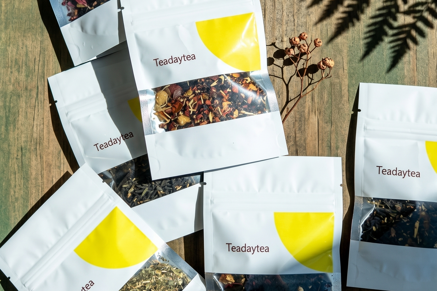 An assortment of Teadaytea small-batch organic tea packaging displayed under natural light and botanical shadows.