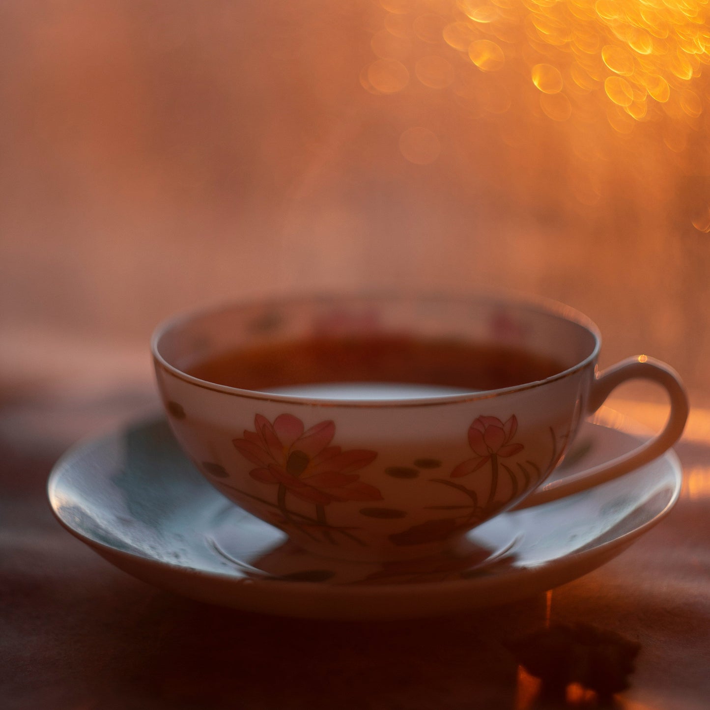 Tea cup with floral design on a saucer against a warm, blurred background